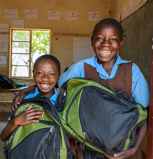 two children smiling carrying backpacks